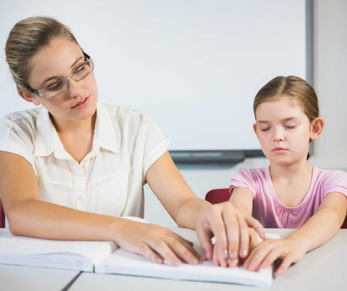 A woman helping a child read brail