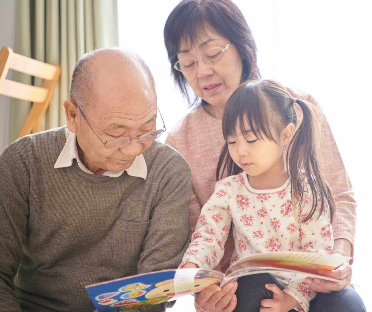 Two adults with a child happily reading a book together