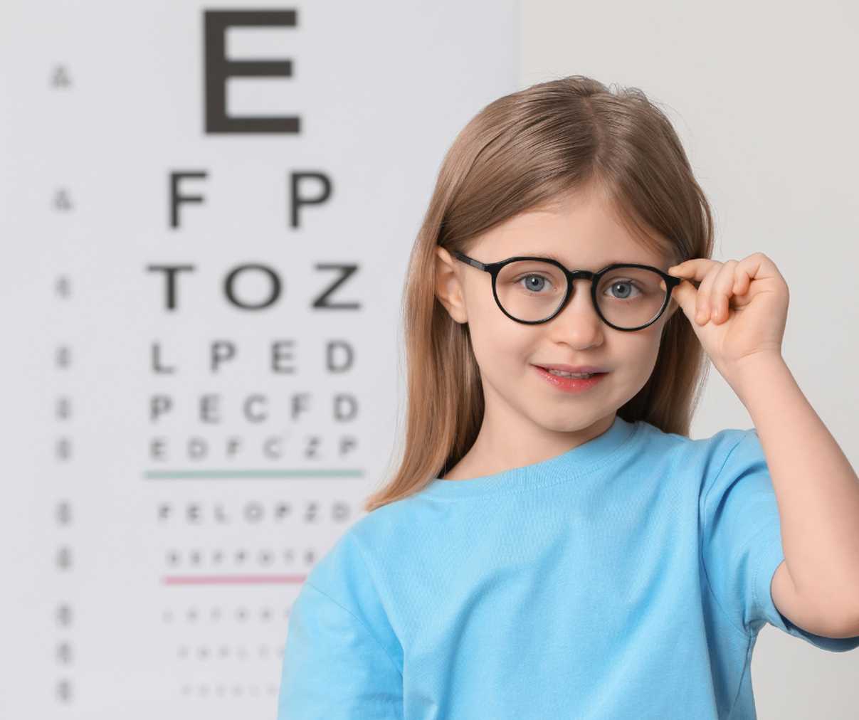 Girl Smiling Next To Eye Testing Exam Equipment